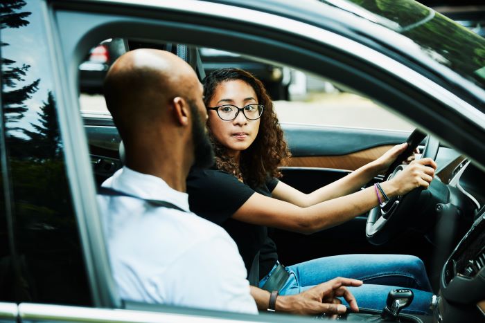 a young woman driving with her parent