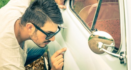 a man inspecting a scratch on the side of a car