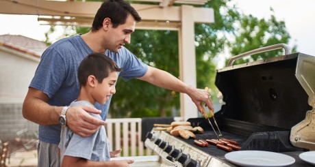 a father and his son turning hot dogs on the grill