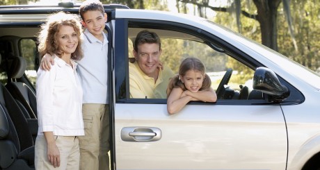 un hombre, su esposa y sus hijos sonriendo y mirando por la ventana de su minivan