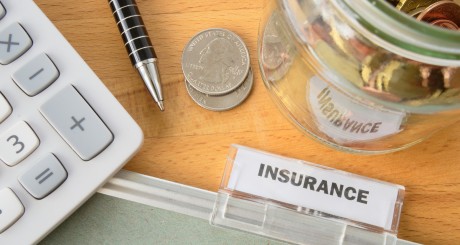 a calculator, a pen, an insurance folder, and some quarters resting on a desk