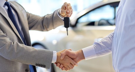 a care salesperson handing the key over to the purchaser of a new car