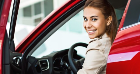 a smiling woman opening the door of her red car