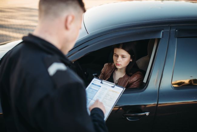 a young woman who looks sad because she was pulled over by a police officer with a clipboard
