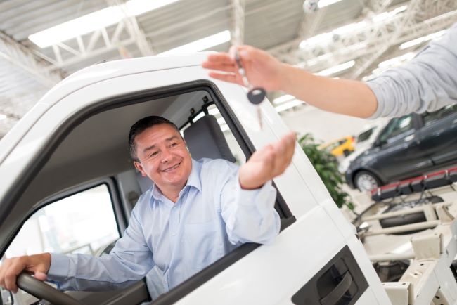 a man in a blue button down shirt takes car keys from a car salesman through the open window of his new truck