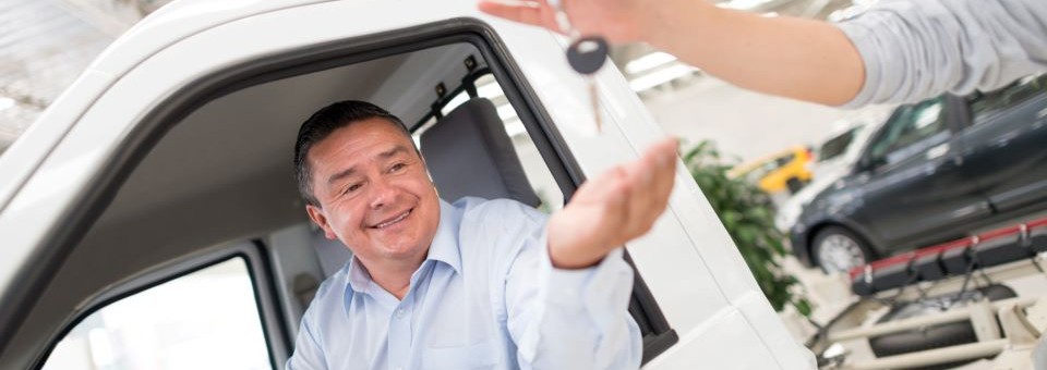 a man in a blue button down and white truck takes car keys from the man selling the car to him